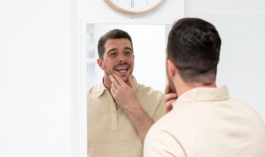 muškarac se gleda u ogledalo, gleda zube