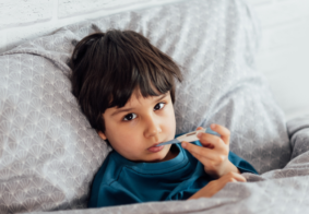 dječak leži u krevetu s termometrom u ustima