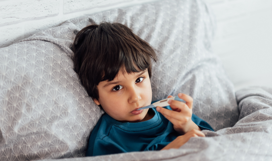 dječak leži u krevetu s termometrom u ustima