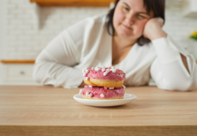 debela žena gleda u krafnu na stolu
