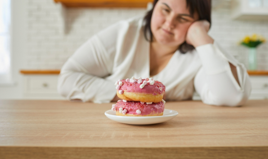 debela žena gleda u krafnu na stolu