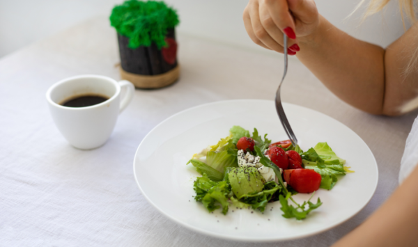 krupni kadar žene koja jede salatu posluženu na bijelom tanjuru