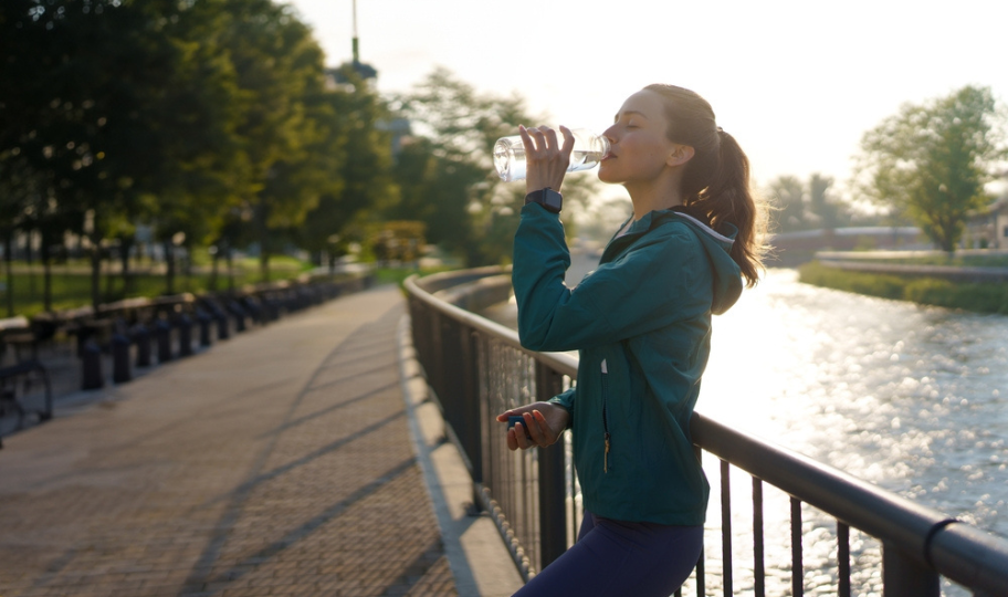 mlada žena pije vodu uz rijeku nakon treninga